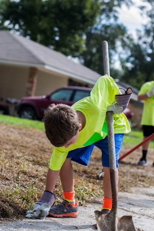 A child in a safety vest picking up debris.