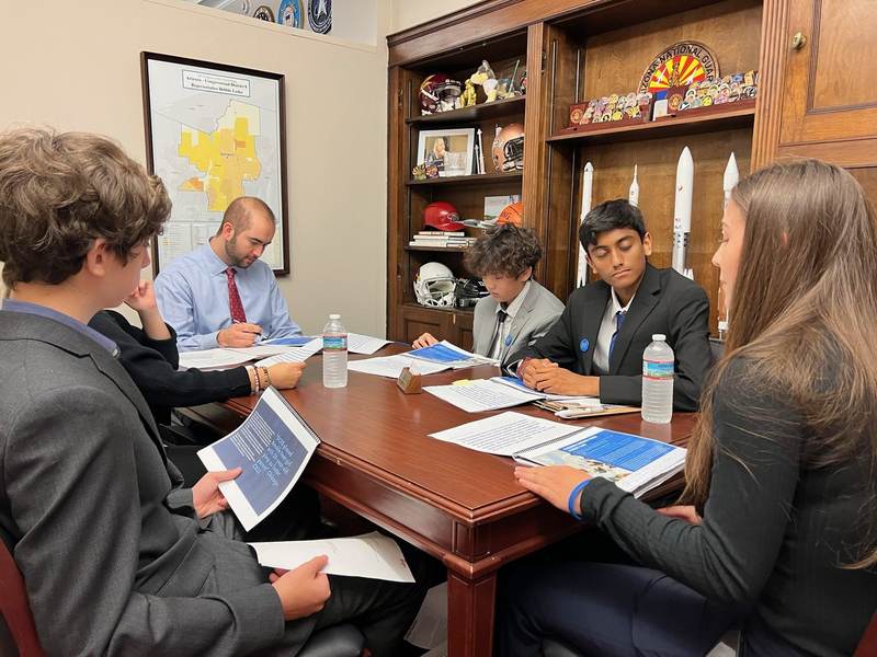 Students in a briefing, folders open on the table.