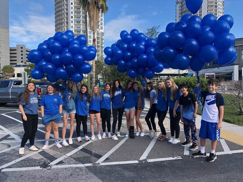 See Us Now members with blue balloons in a parking lot.